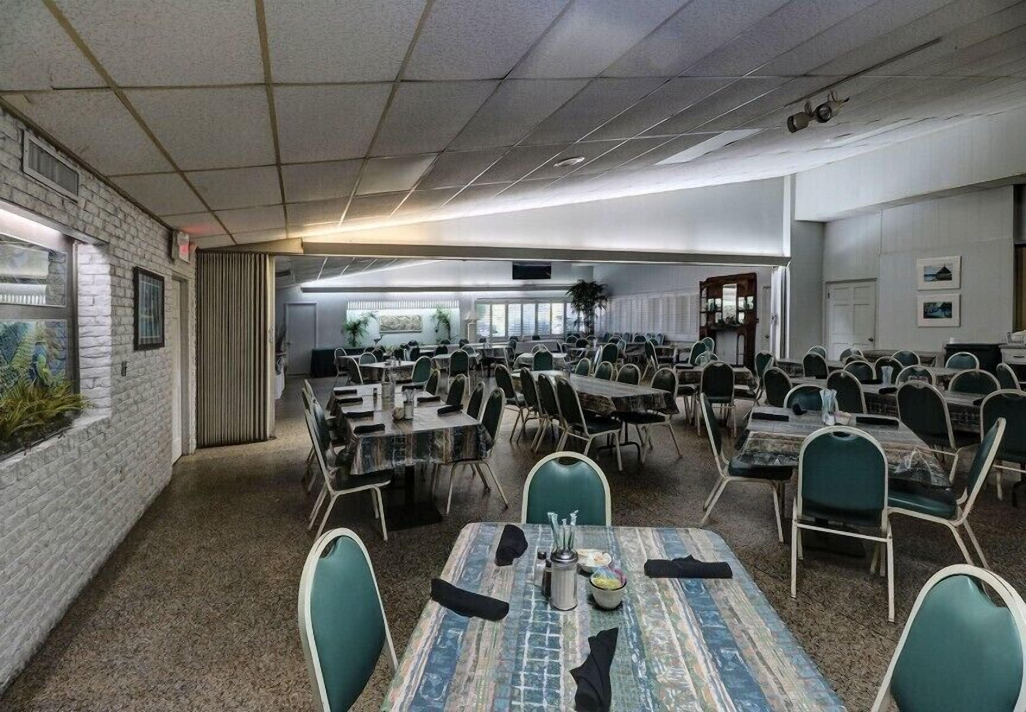 A conference room with multiple tables and chairs, a brick wall with a window, and a ceiling with recessed lighting.