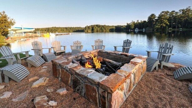 Eine Seeterrasse mit Adirondack-Stühlen, einem Steinkamin und Blick auf den See.