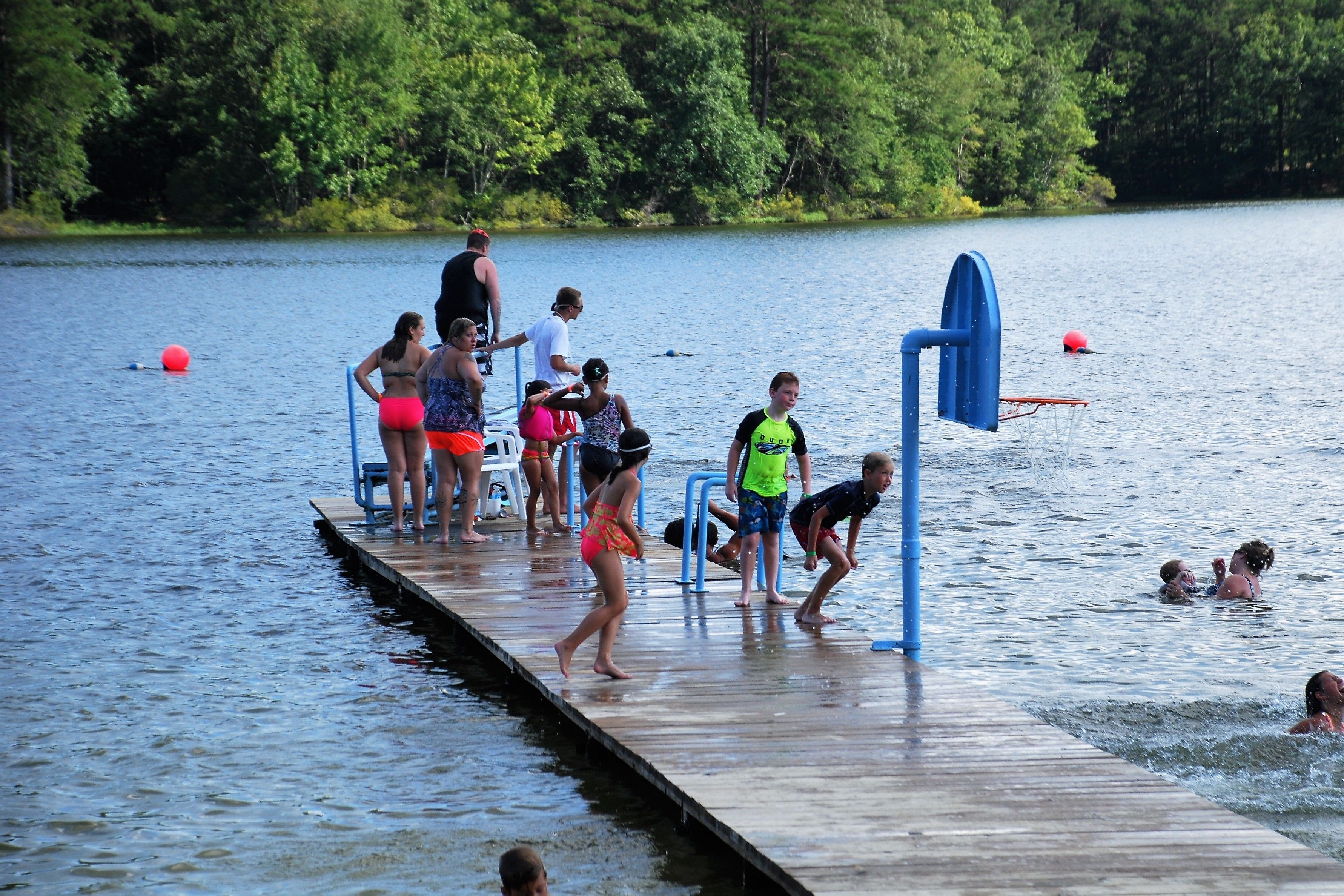 A wooden dock extending into a lake with people standing and walking on it.