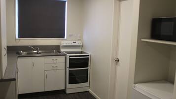 A compact kitchen with white cabinets, a built-in oven, a microwave on a shelf, and a window above the sink.