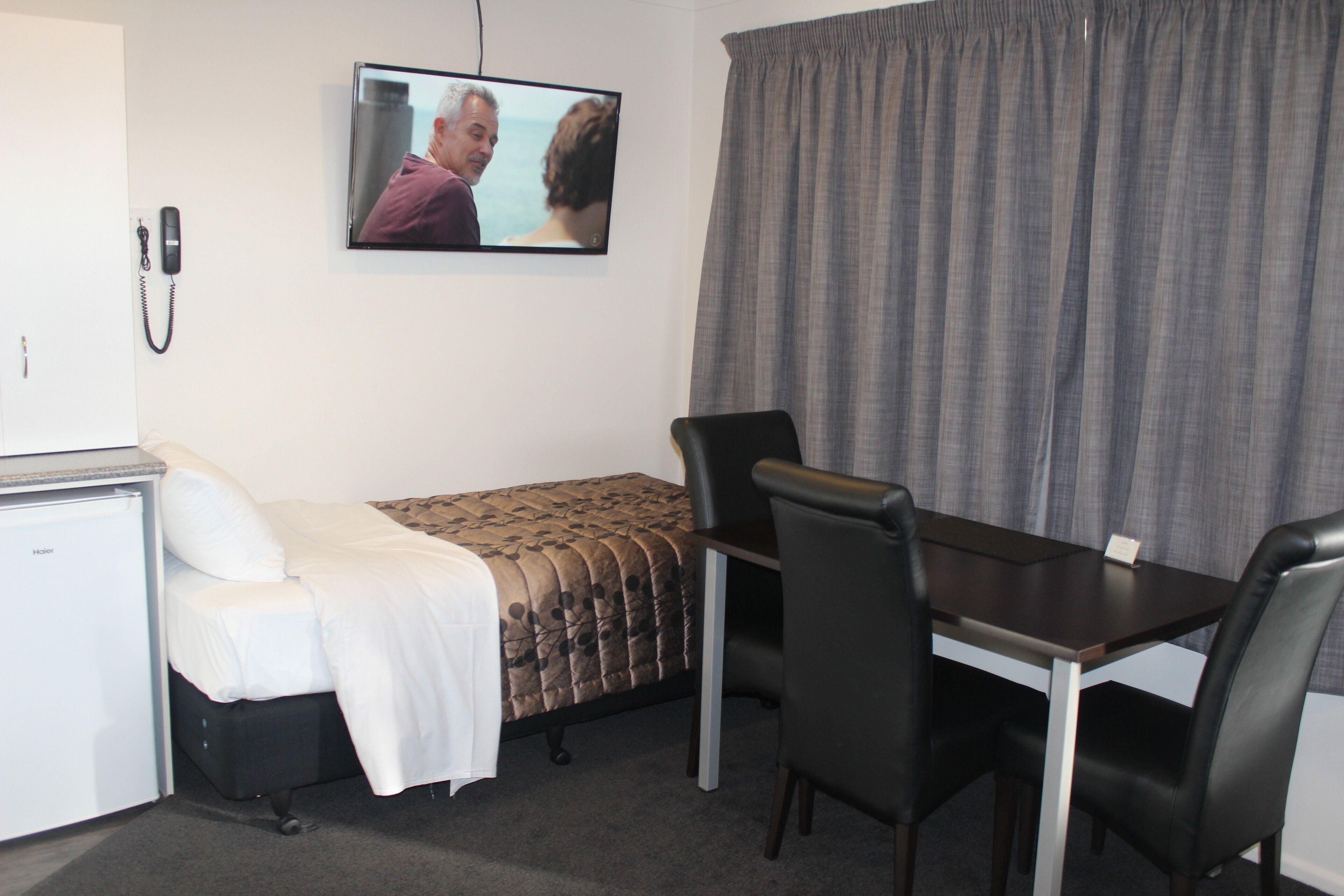 Une chambre d’hôtel comprenant un lit, un bureau, deux chaises, une télévision et un téléphone.
