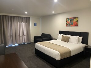 A hotel room with a large bed, a black headboard, a black sofa, a small table, and a painting on the wall. -  Riverlea Motel (Gore)