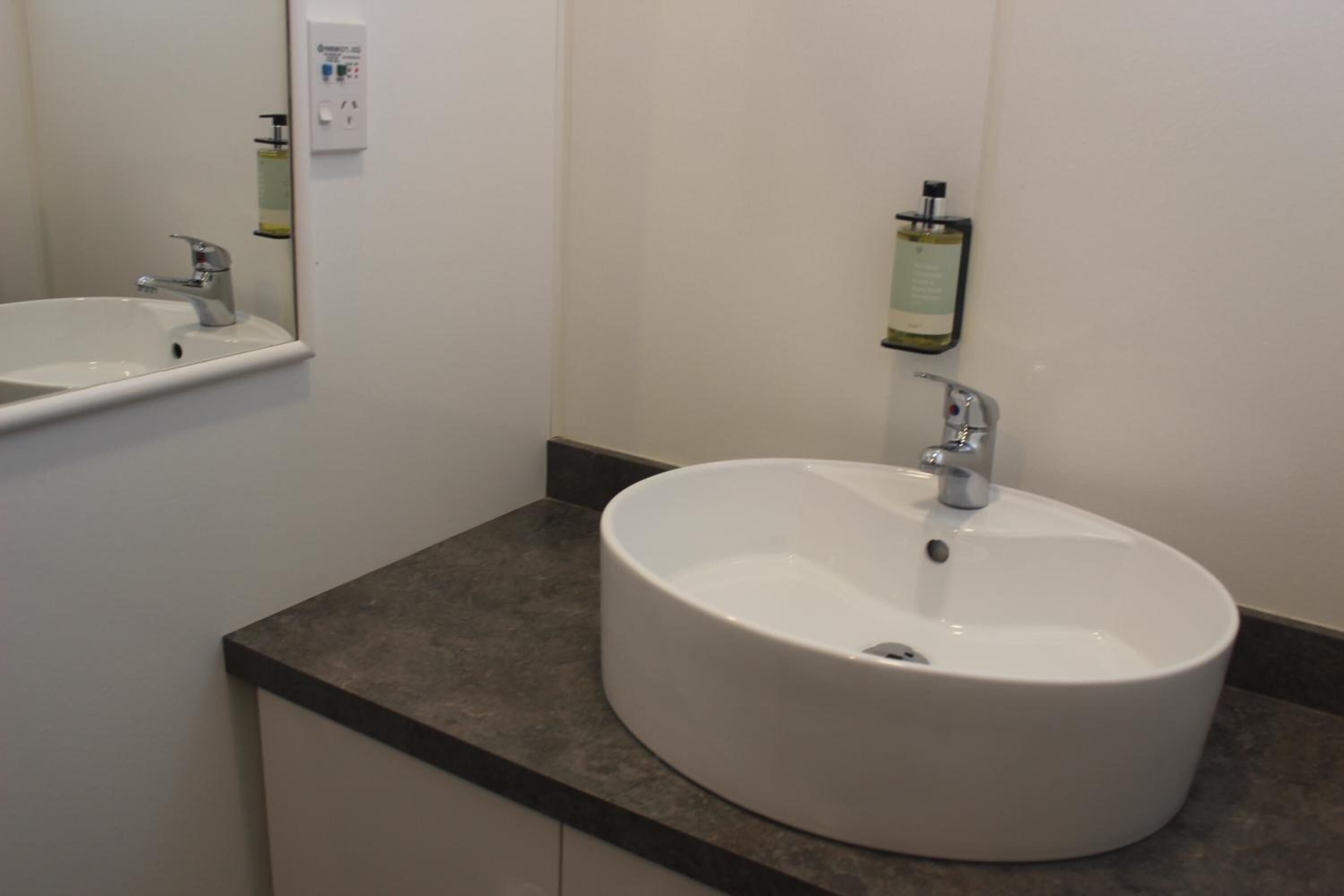 A bathroom with a white sink, a mirror, and a soap dispenser on the wall.