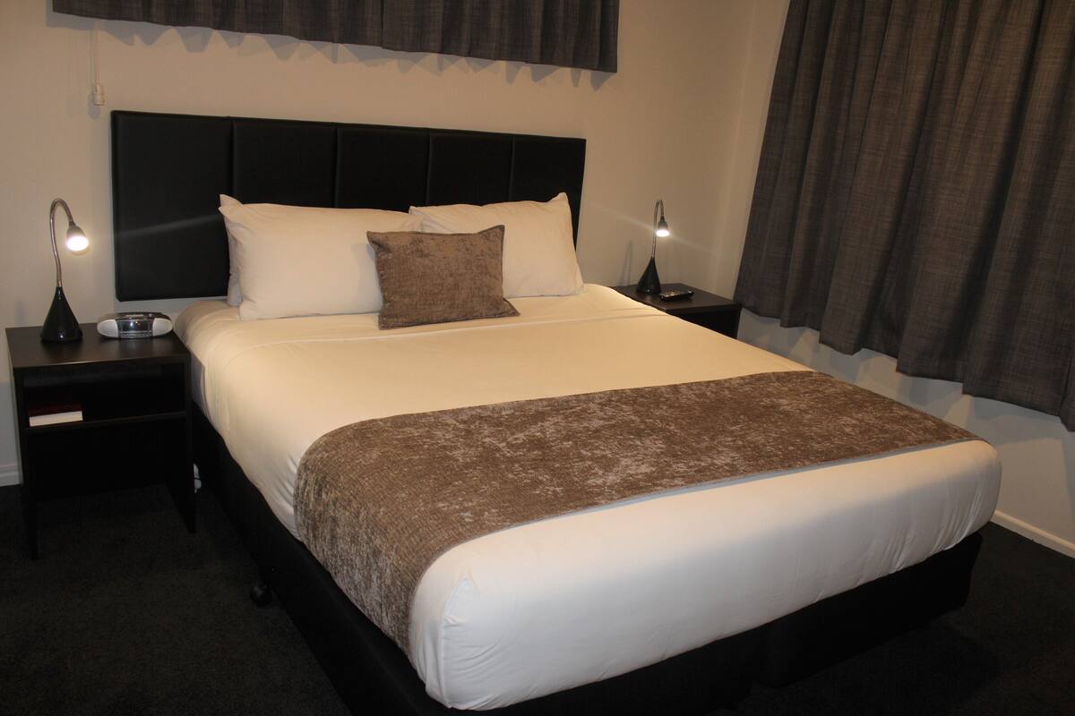 A neatly made bed with white and brown linens, two bedside tables with lamps, and a dark headboard.