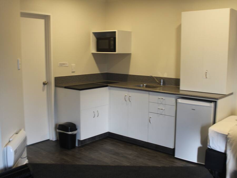 A compact kitchen with white cabinets, a microwave, a small refrigerator, and a sink.