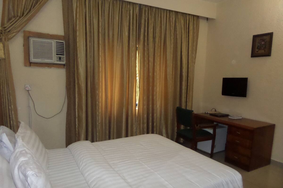 Una habitación de hotel con cama, escritorio, silla, televisor y cortinas.