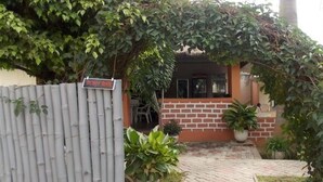 Une maison avec une clôture en bambou, une façade en briques et des plantes en pot.