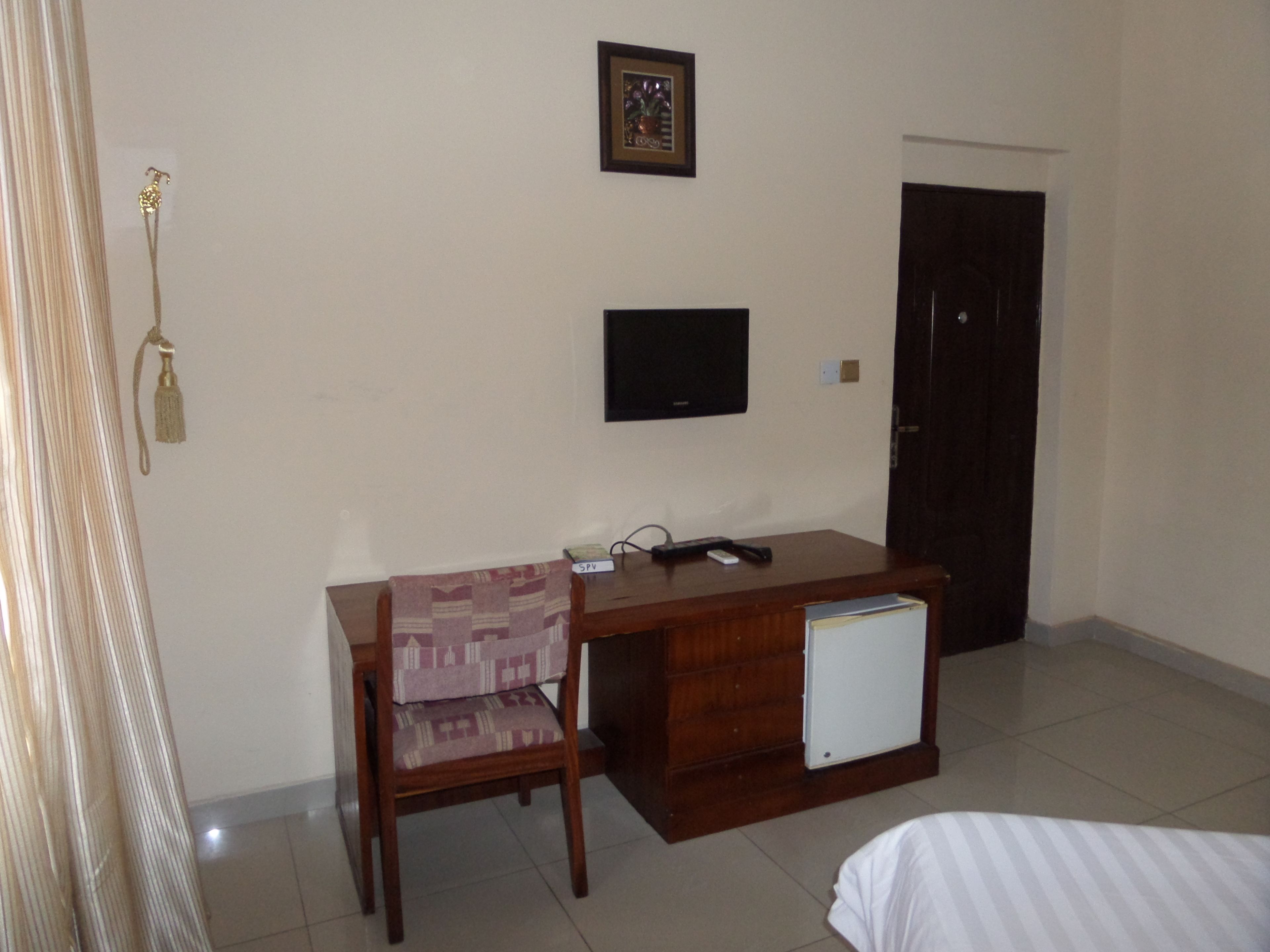A hotel room with a wooden desk, a chair, a television, and a door.