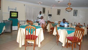 Un espace repas avec des tables disposées pour accueillir plusieurs personnes, des chaises, un téléviseur et un ventilateur de plafond.