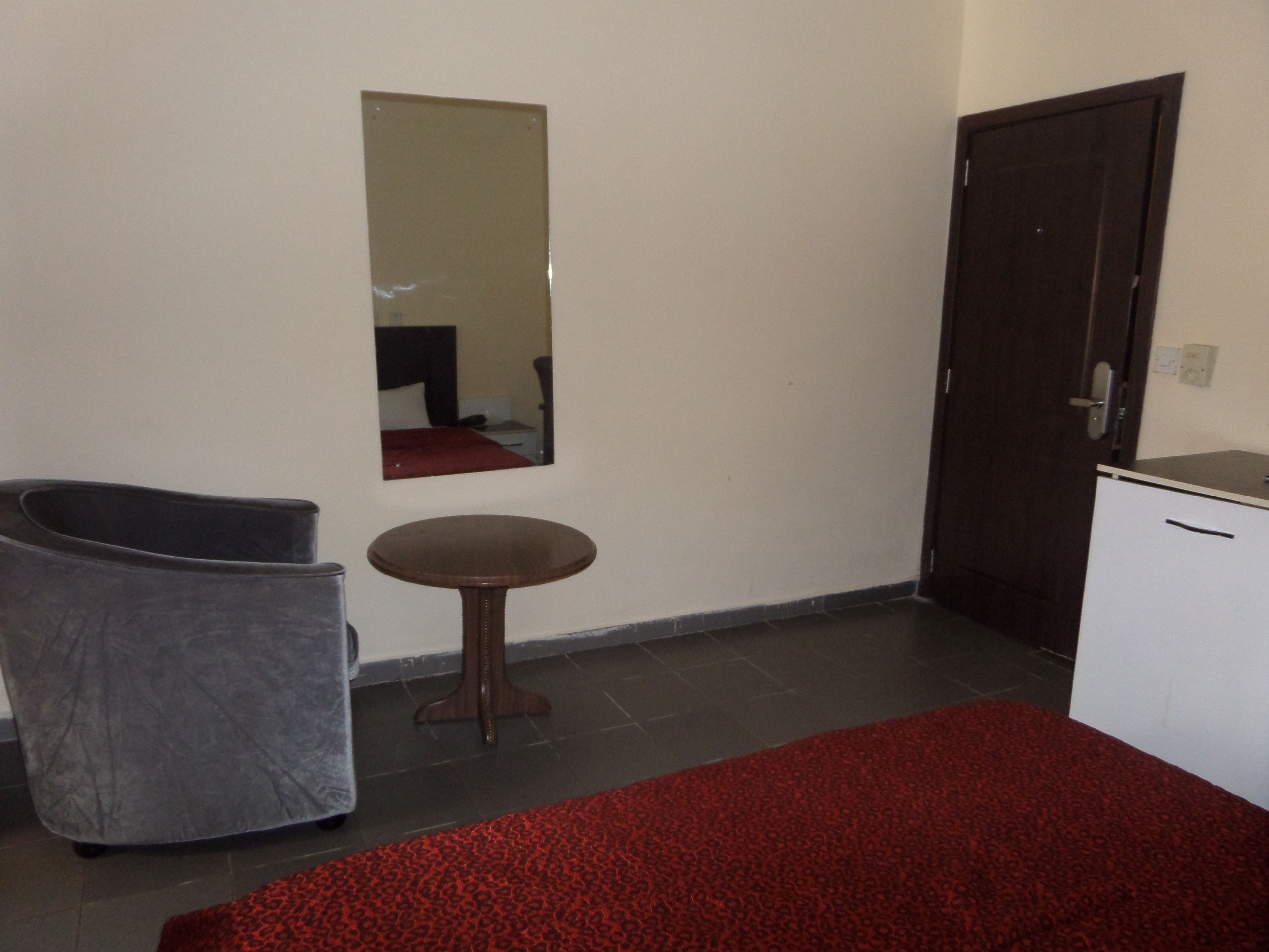 Una habitación con una cama, una silla, una mesita, un espejo y una puerta.
