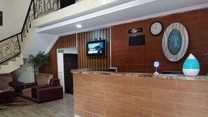 A reception area with a reception desk, a television mounted on the wall, a clock, and a staircase in the background. - Dreamland Suites (Abuja)