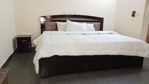 A neatly made bed with white bedding in a room with a dark wooden headboard. - Dreamland Suites (Abuja)