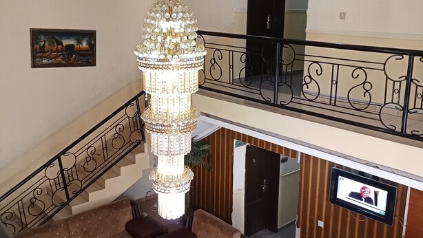 A spacious lobby with a grand chandelier, a staircase, and a flat-screen TV mounted on the wall. - Dreamland Suites (Abuja)