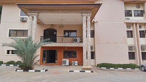 A multi-story building with a covered entrance, air conditioning units, and a small garden area. - Dreamland Suites (Abuja)