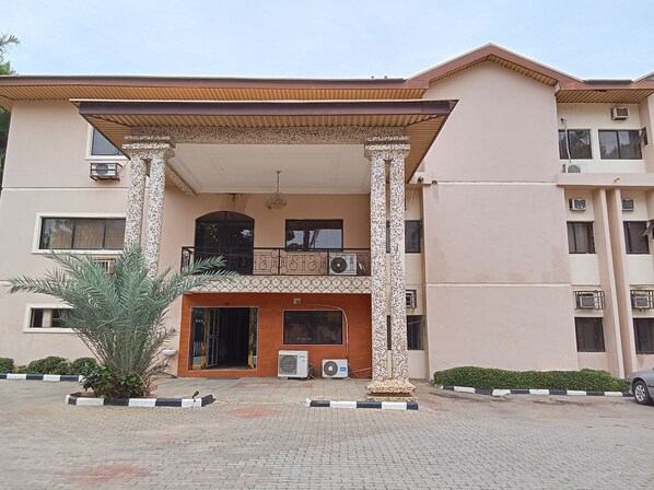A multi-story building with a covered entrance, air conditioning units, and a small garden area. - Dreamland Suites (Abuja)