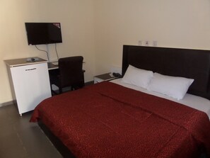 A hotel room with a bed, a desk, a chair, a TV, and a small refrigerator. - Dreamland Suites (Abuja)