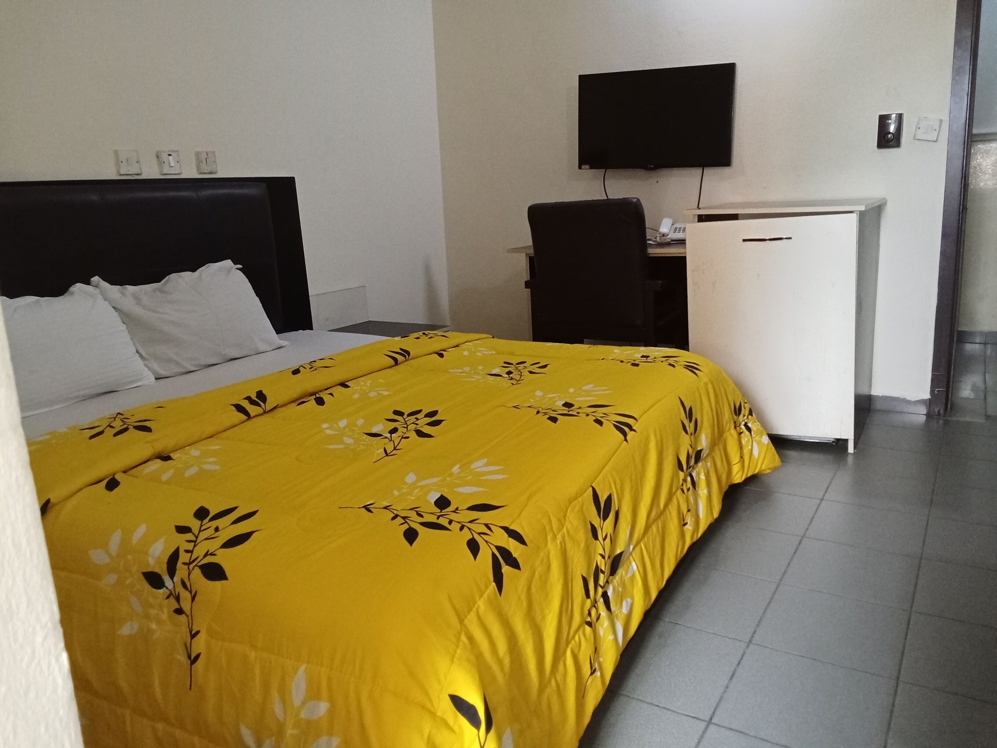 Quarto de hotel com cama, escrivaninha, cadeira, televisão e telefone.