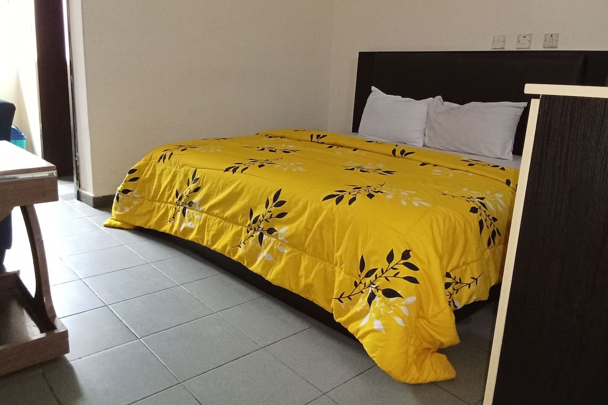 A bed with a yellow floral bedspread, a wooden headboard, and white pillows.