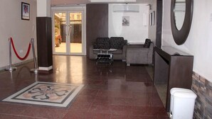 Un vestíbulo de hotel con mostrador de recepción, zona de estar y entrada por puerta de vidrio.
