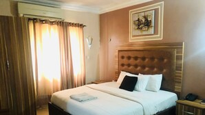 Habitación de hotel con una cama grande, cabecera de madera, mesita de noche con teléfono y un cuadro en la pared.