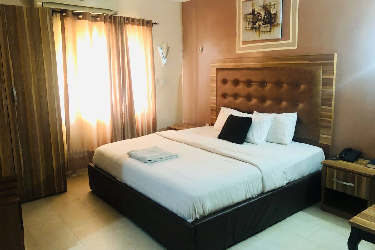 A hotel room with a large bed, a wooden headboard, a bedside table with a phone, and a painting on the wall.