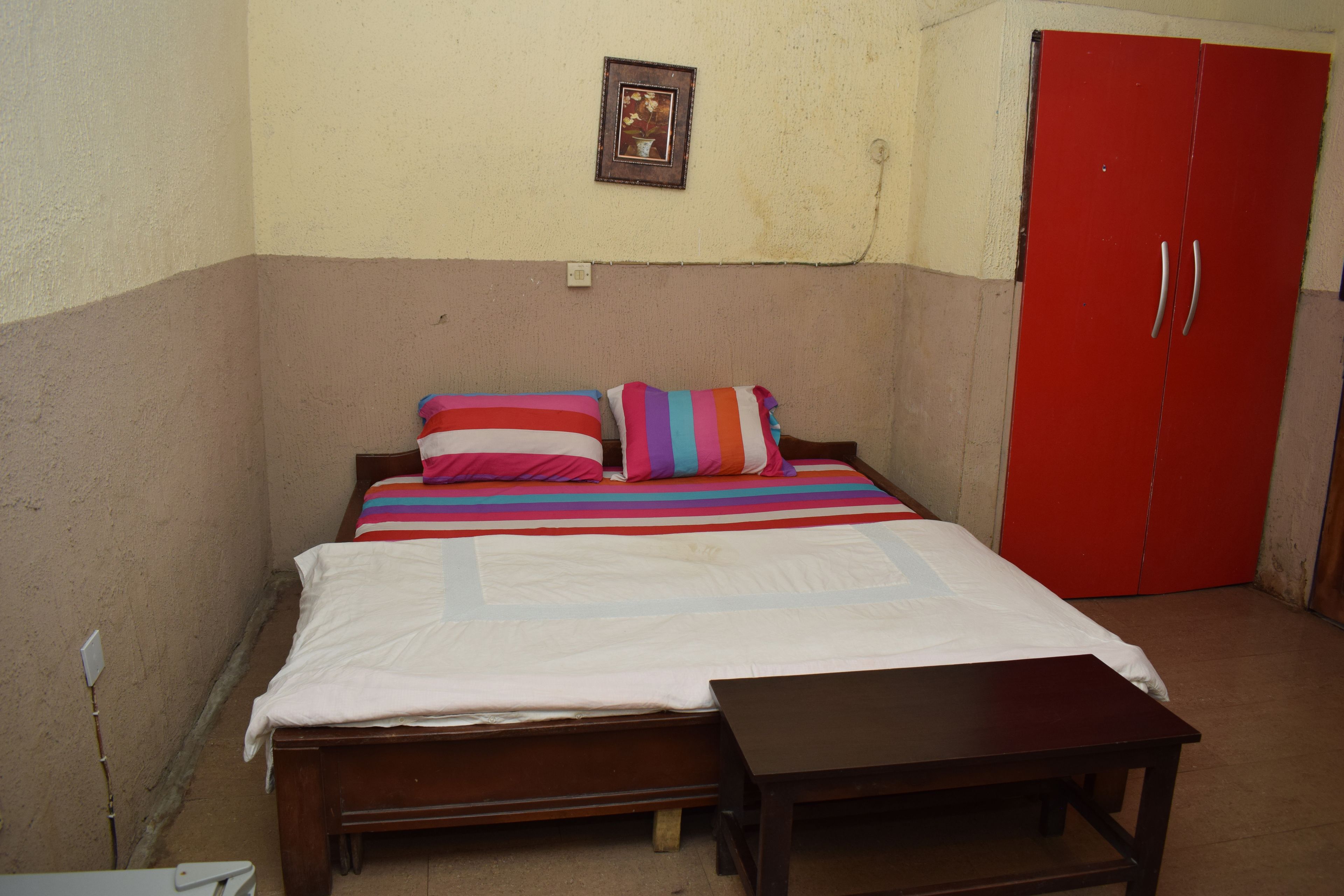Une chambre à coucher avec un lit, une table de chevet, une armoire rouge et un tableau accroché au mur.