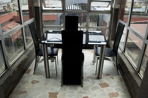 Ein Eckzimmer mit Tisch und vier Stühlen, großen Fenstern und einem Fliesenboden.