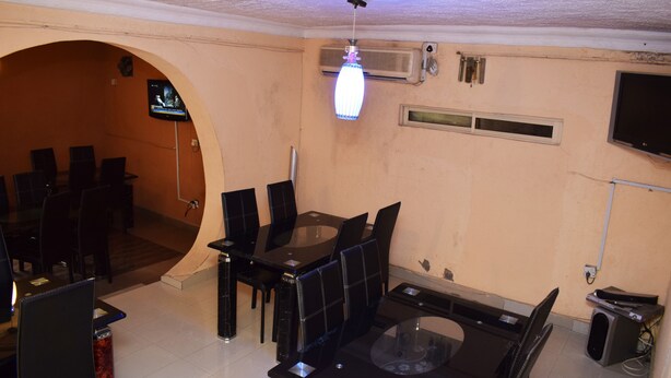 A dining area with a glass table and black chairs, an air conditioning unit, and a television mounted on the wall. - Wazobia Plaza Hotel (Lagos)
