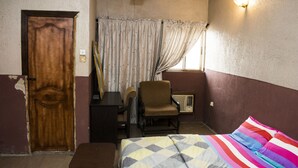 A bedroom with a bed, a chair, a desk, and a window with curtains. - Wazobia Plaza Hotel (Lagos)
