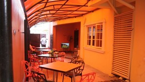 An outdoor dining area with tables and chairs, a television, and a person in the background. - Blue Seasons Hotel & Suites (Lagos)