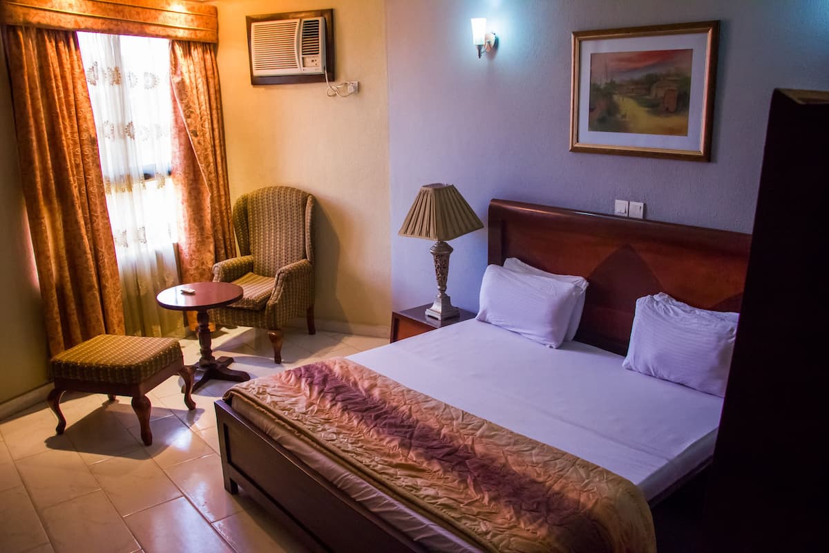 Ein Hotelzimmer mit Bett, Stuhl, kleinem Tisch, Lampe und einem Bild an der Wand.