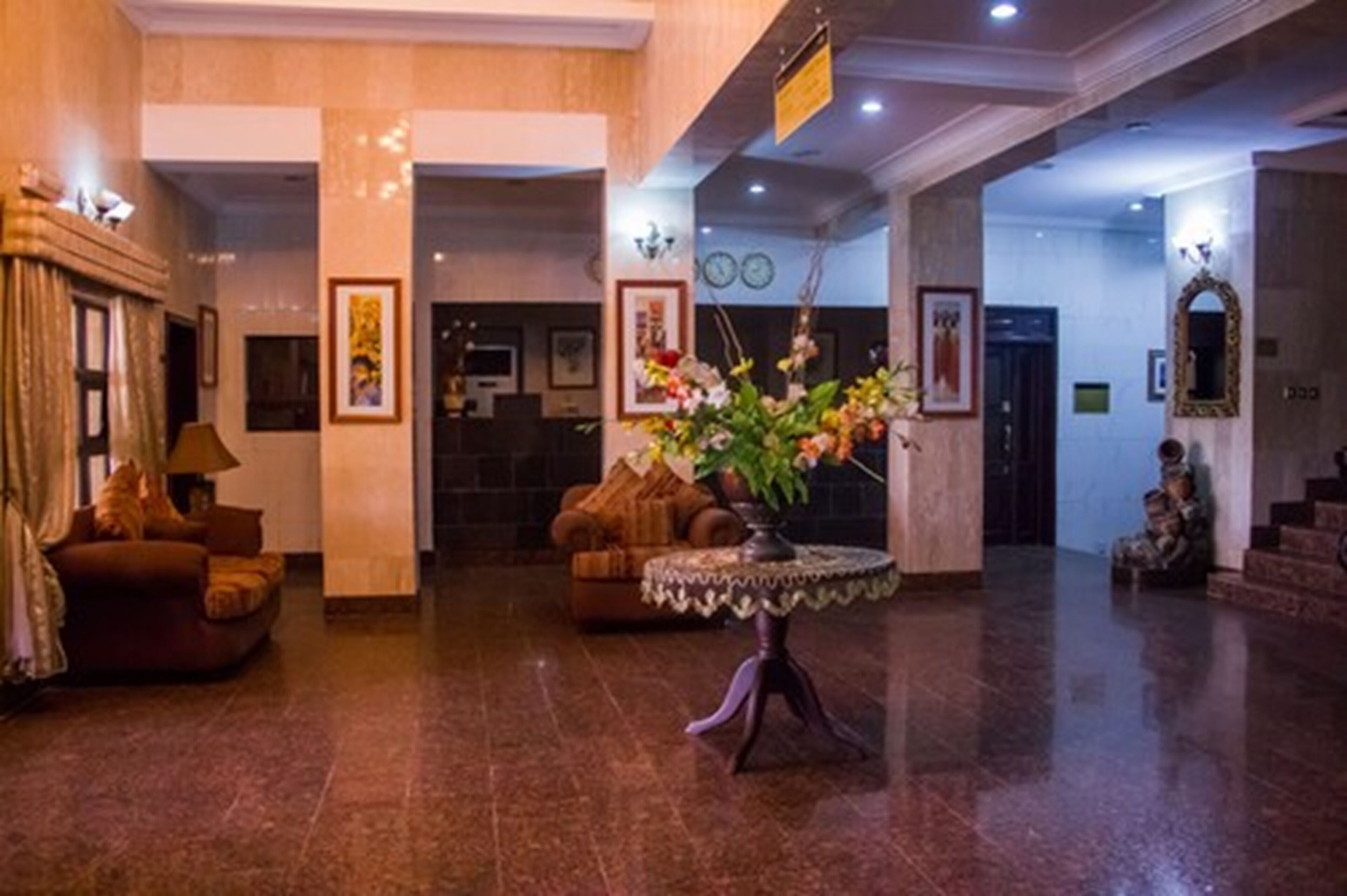 A lobby with a reception desk, two sofas, a coffee table with flowers, and a staircase.