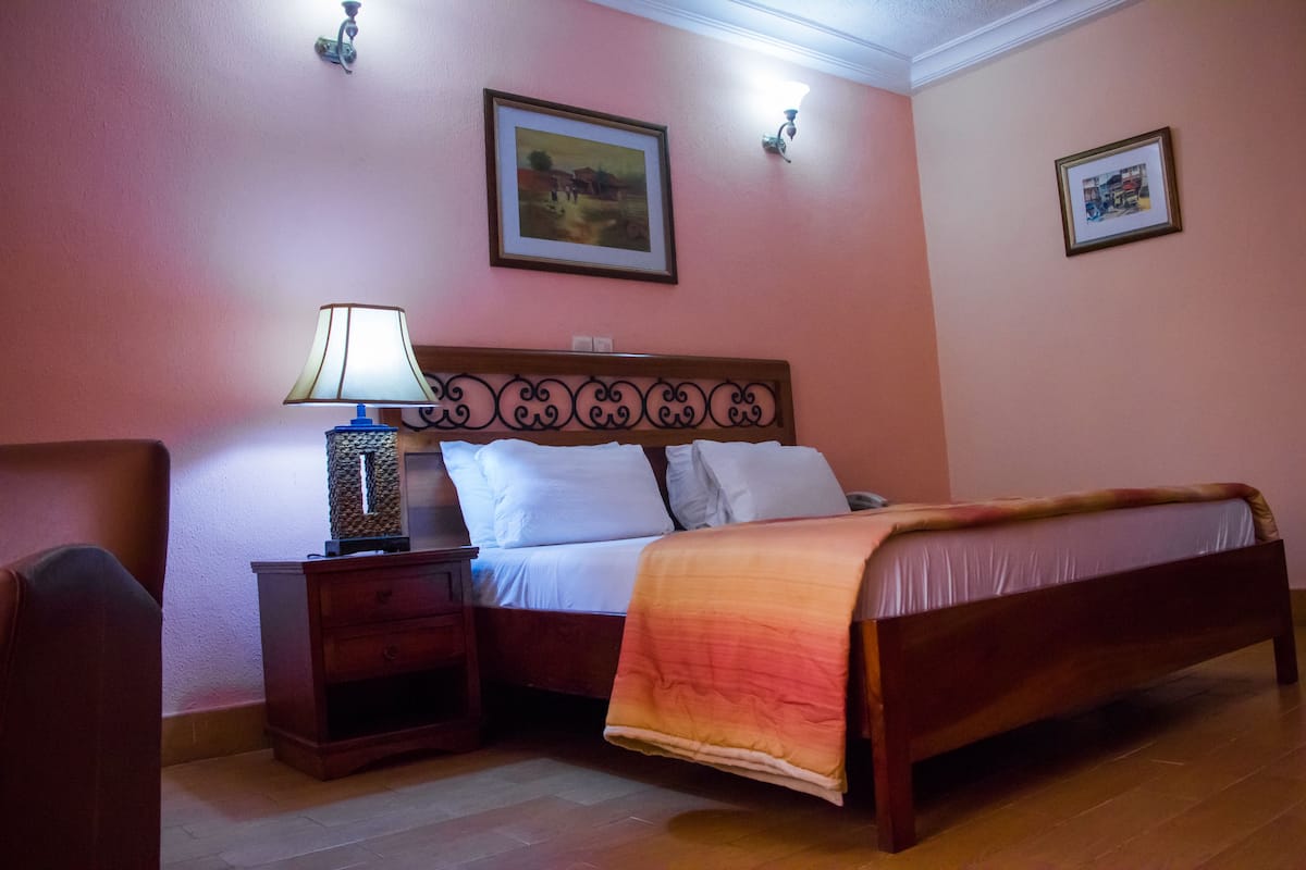 Ein Schlafzimmer mit einem hölzernen Bett, einem Nachttisch mit Lampe, einem Sessel und zwei gerahmten Bildern an der Wand.
