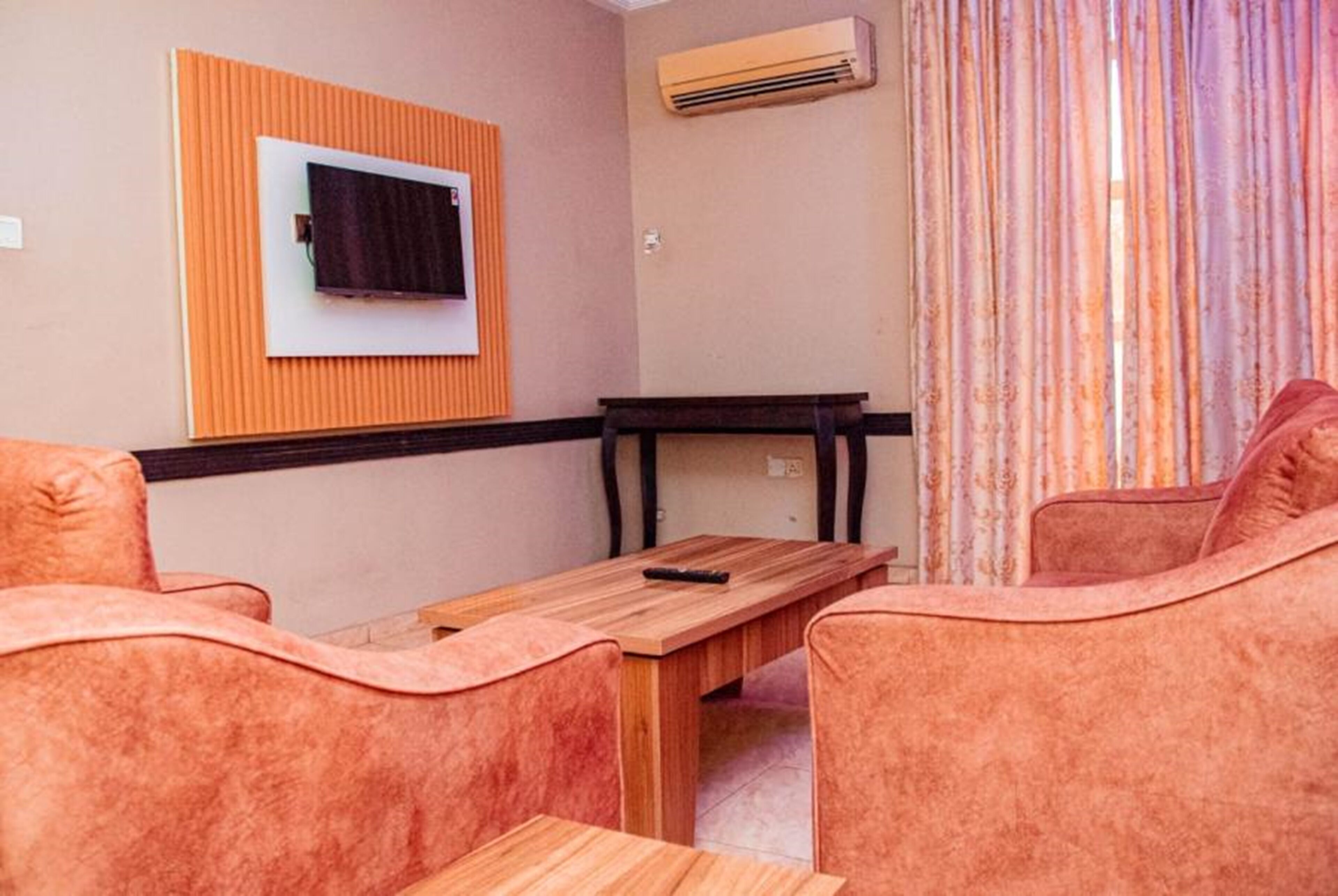 A room with a wooden table, two cushioned chairs, a mounted TV, and an air conditioning unit.