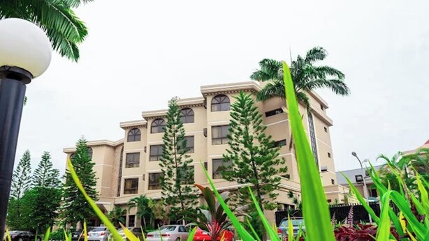 A multi-story building with a symmetrical facade, surrounded by greenery and parked cars. - Dees Hotels, Apartments and Suites (Lagos)