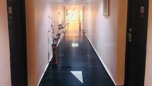 Un pasillo de hotel con suelo de baldosas negras, una planta en maceta y puertas con las indicaciones 106 y 107.