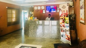 Zona de recepción de un hotel con un mostrador de mármol, una pantalla de televisión y un reloj en la pared.