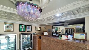 Zona de recepción de un hotel con mostrador de mármol, certificados enmarcados y una araña.