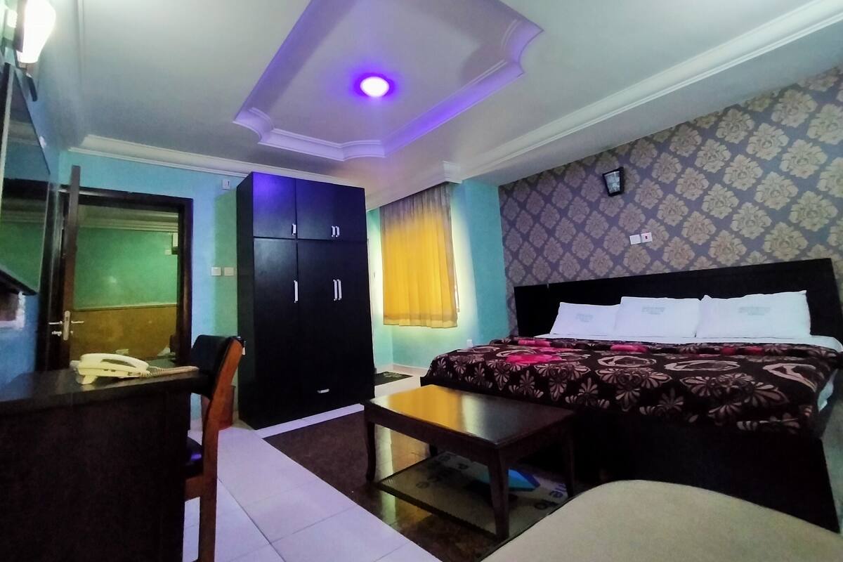 Une chambre d’hôtel avec un lit, un bureau, une armoire et un luminaire au plafond.