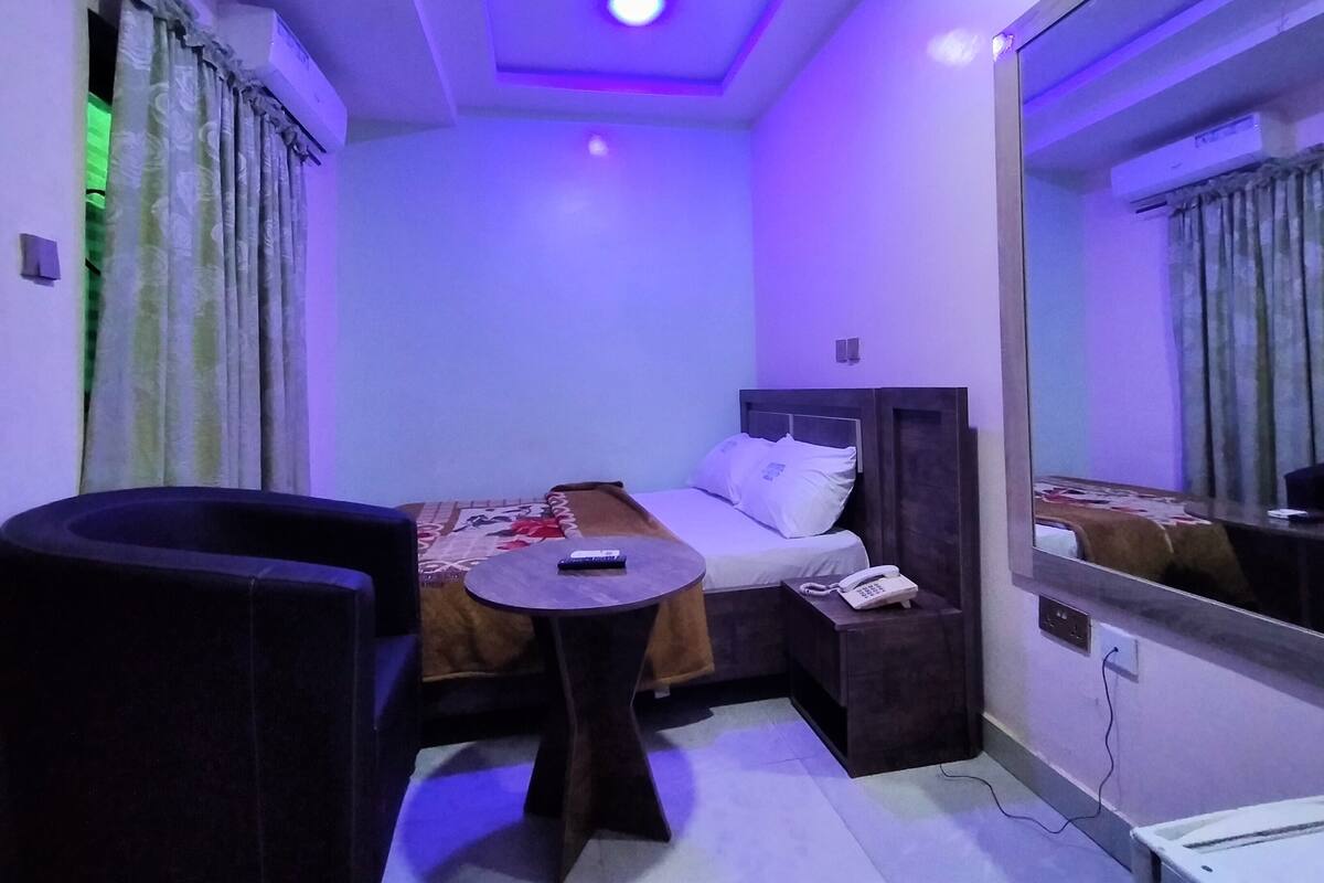 Une chambre d’hôtel de taille réduite, comprenant un lit, une table de chevet et une petite table avec une télécommande.