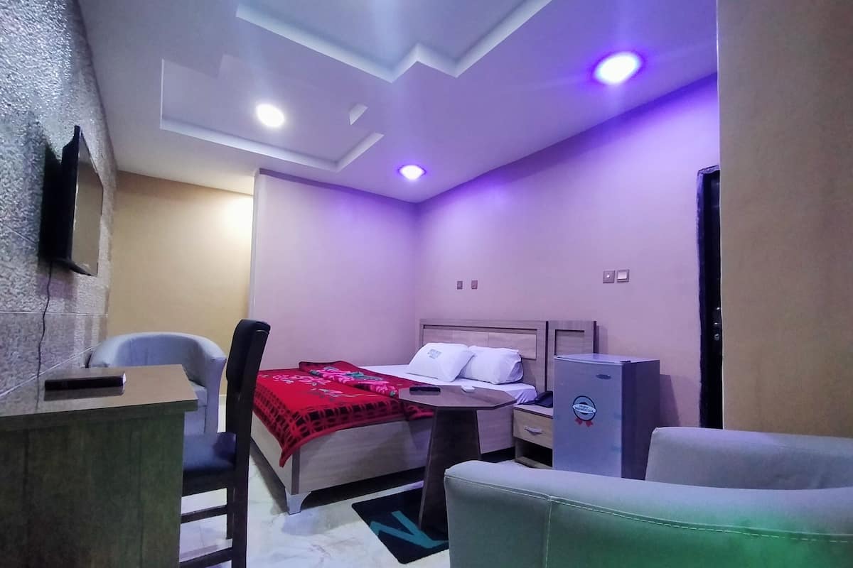 Une chambre d’hôtel équipée d’un lit, d’un bureau, d’une chaise, d’une armoire et d’un téléviseur fixé au mur.