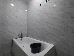 A bathroom with a marble wall and floor, a white bathtub, and a black bucket. - Orient Hotel & Plaza (Abuja)