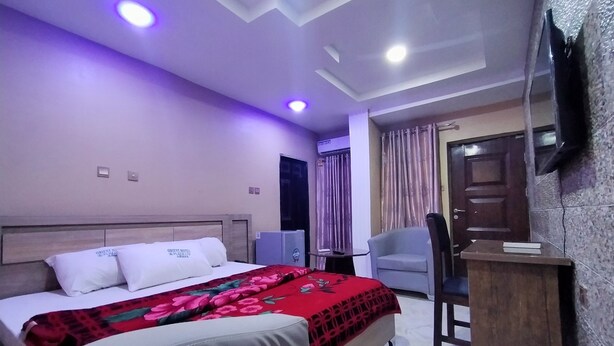 Una habitación de hotel con cama, escritorio, silla, televisión y aire acondicionado.