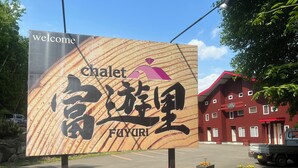 A welcome sign for a hotel named 'Chalet Fuyuri' with a red building in the background. - Chalet Fuyuri (Furano)