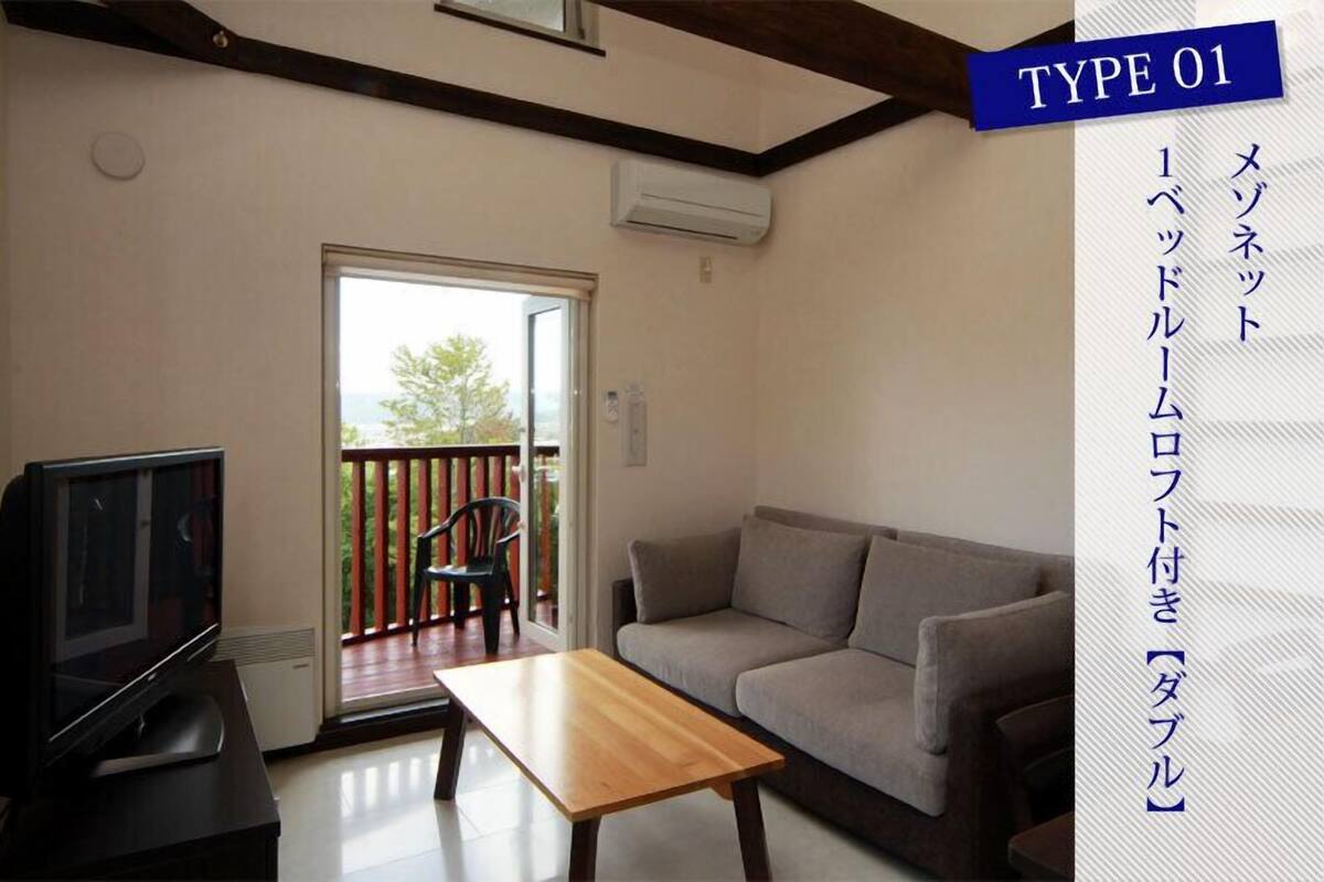 A living room with a sofa, a TV, and a table. There is a sliding door leading to a balcony.