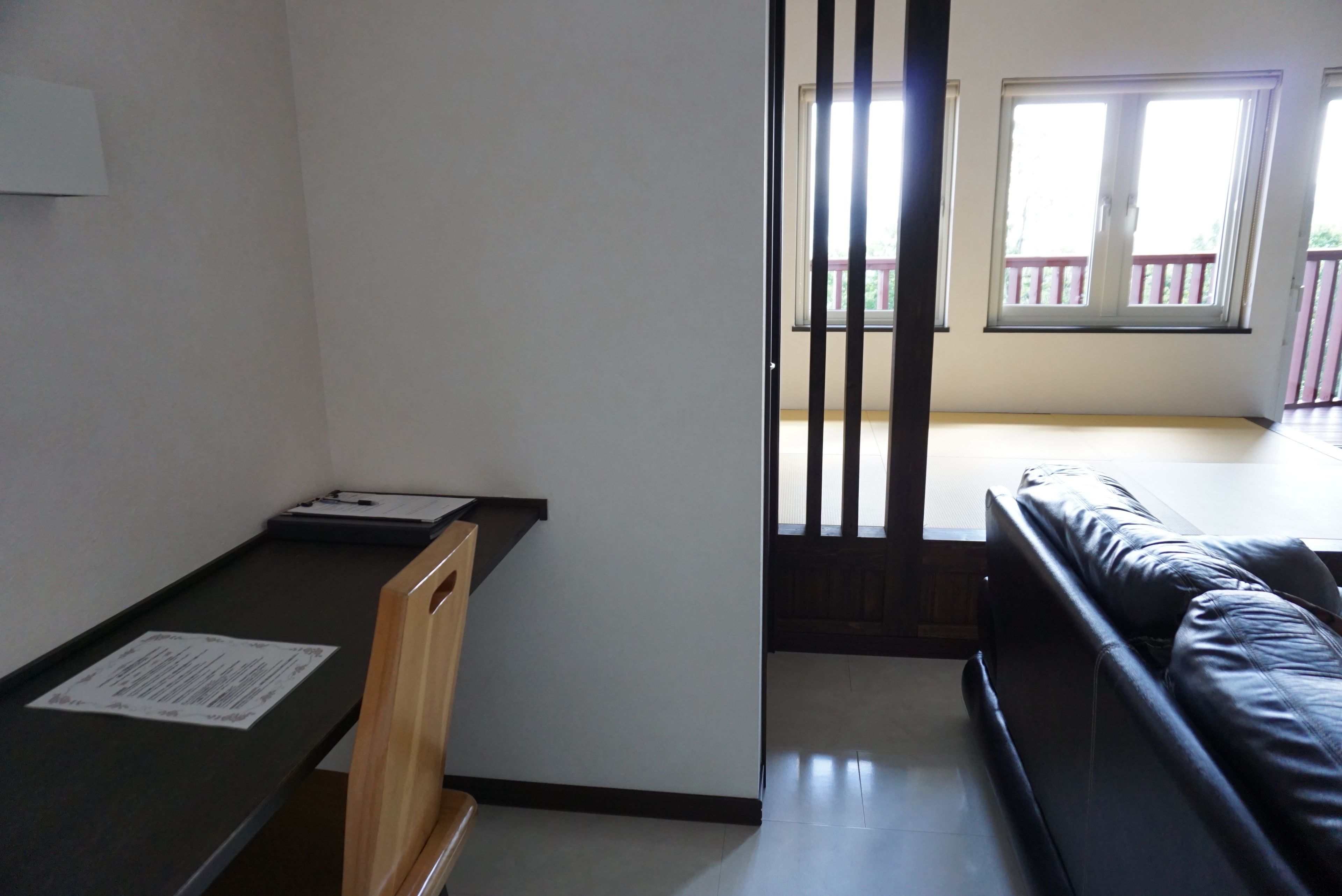 Una habitación con un escritorio, un sofá de cuero negro y un ventanal corredera que da a un balcón.