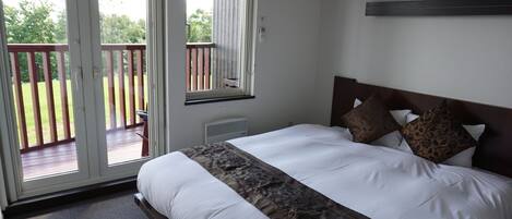Un dormitorio con una cama grande, un balcón con baranda de madera y vistas a la vegetación.