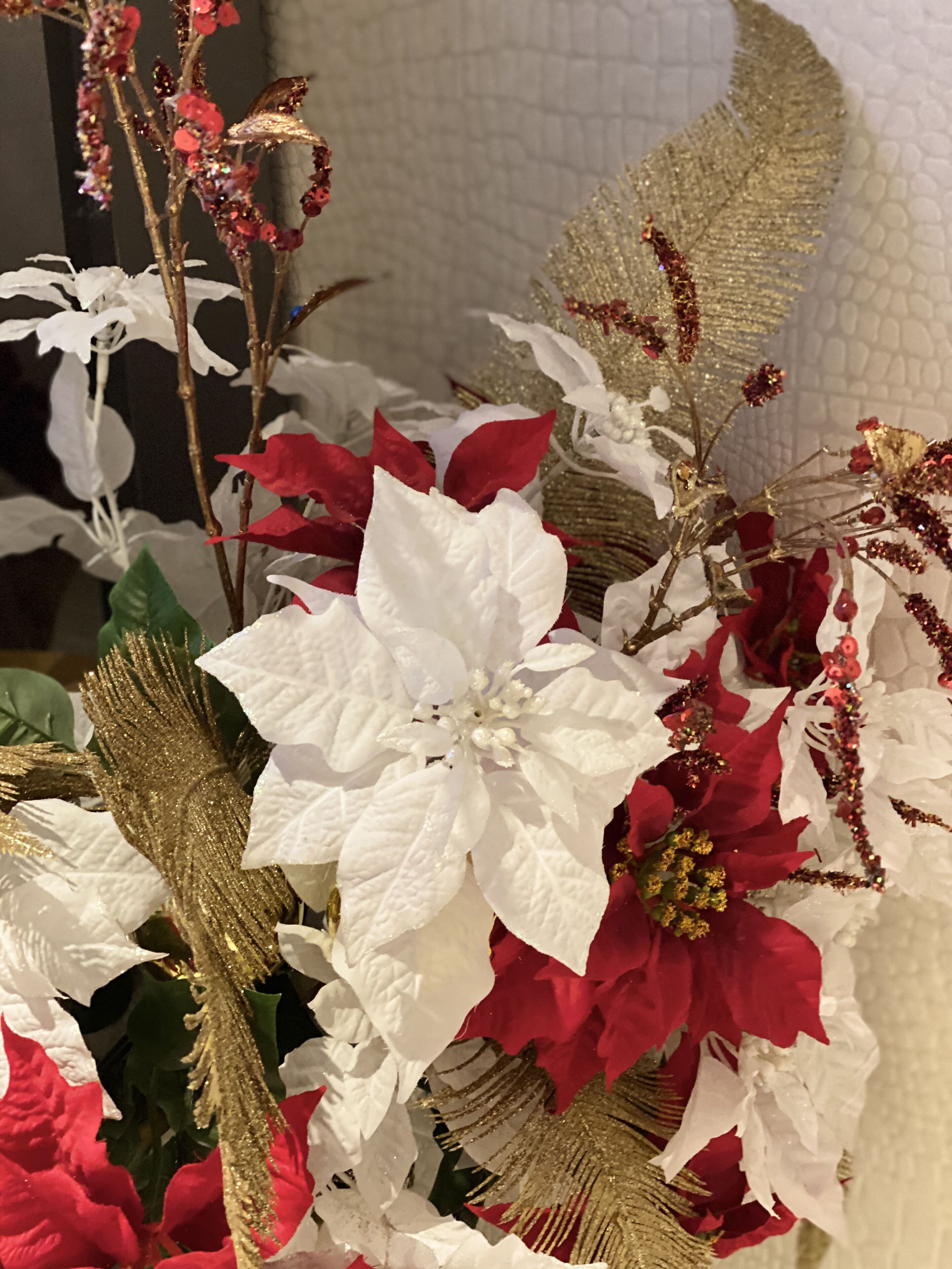 A decorative arrangement with white and red poinsettia plants, gold accents, and a textured wall background.