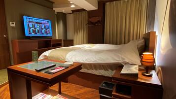 Ein Hotelzimmer mit Bett, Nachttisch, Lampe, Fernseher und Holzboden.