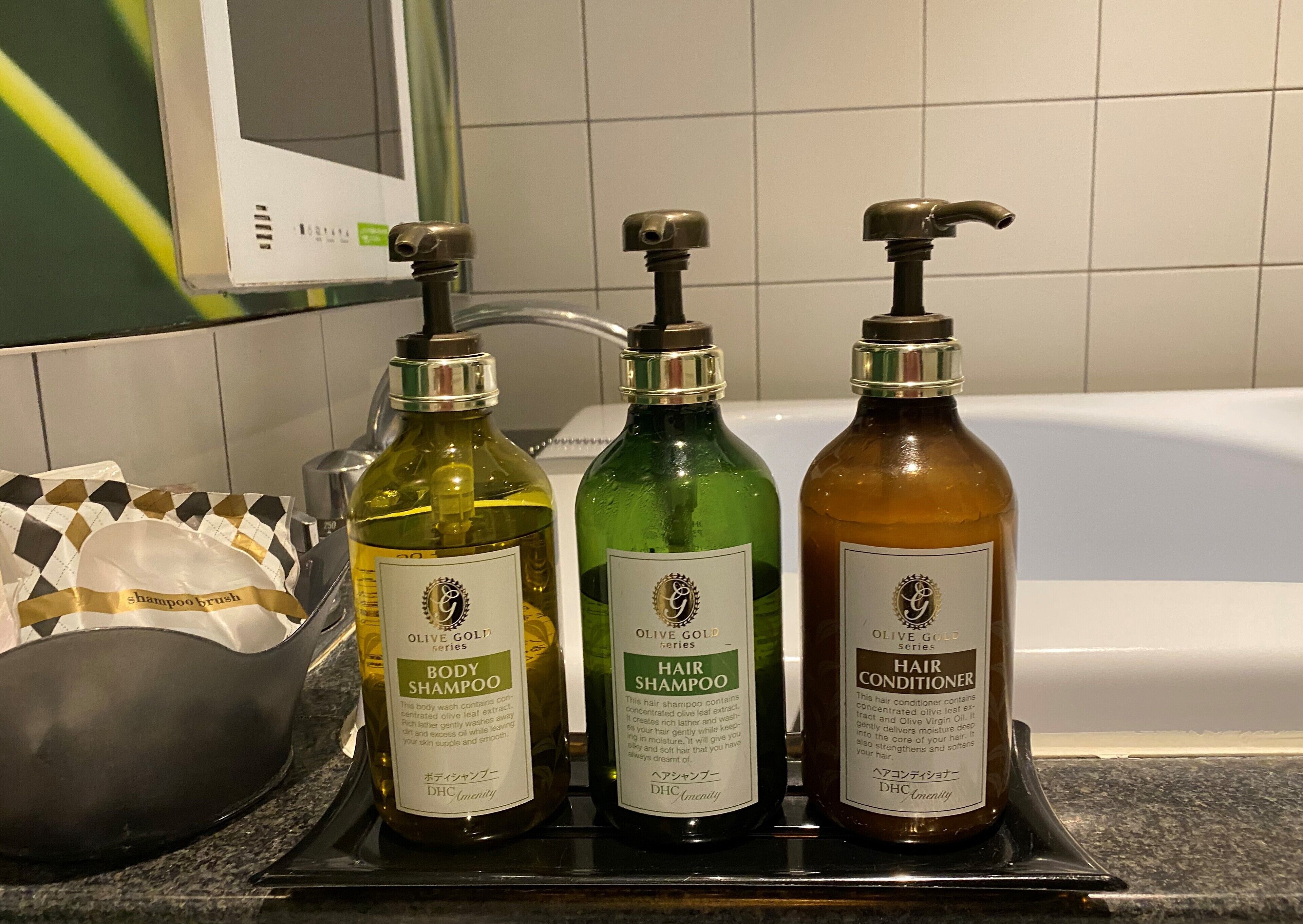 Three bottles of Olive Gold series hair care products on a tray in a bathroom.